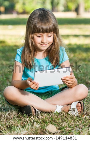 Cute little girl sitting in park and using her tablet computer,Little girl with tablet computer
