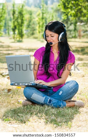 Beautiful woman with headphones sitting in the park and using laptop,Woman with headset using laptop