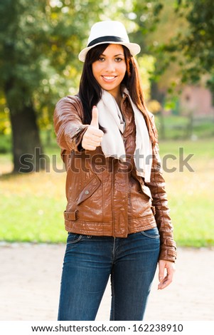Beautiful young woman standing in the park and showing thumb up,Woman showing ok sign