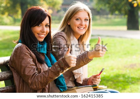 Two students sitting in the park and showing ok sign,Thumbs up for education