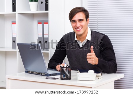 Young businessman sitting in his office and showing thumb up,Successful businessman
