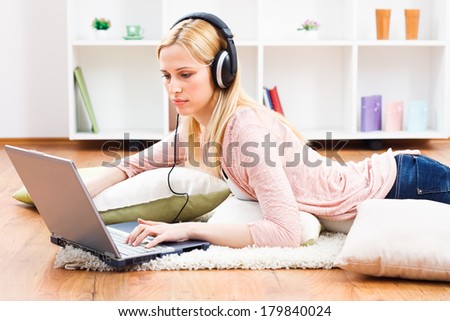Beautiful blonde woman with headphones using laptop at her home,Woman  with headphones using laptop