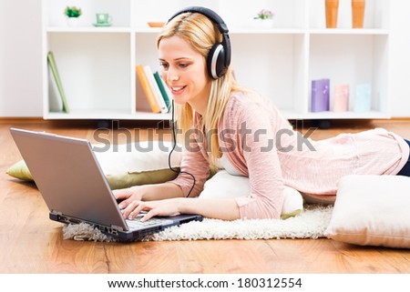 Beautiful blonde woman with headphones using laptop at her home,Woman with headphones using laptop