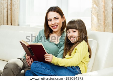 Mother and daughter sitting on sofa at their home and reading a book together,Leisure time for mother and daughter