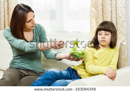 Mother is giving vegetables to her daughter to eat but she is very angry,she don`t like it,I don`t like vegetables!