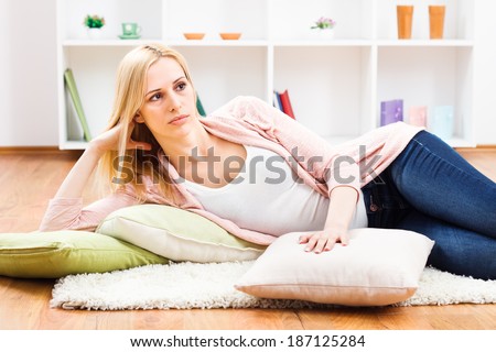 Sad blonde woman lying on carpet in her living room and thinking about something,Sad woman