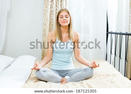 Beautiful blonde woman is meditating on bed in her bedroom,Woman meditating