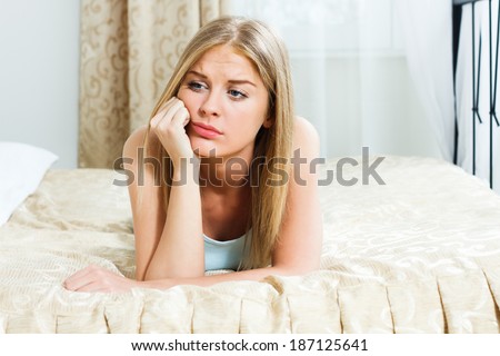 Blonde  woman is lying on  bed in her bedroom and she is very sad because of something,Sad woman