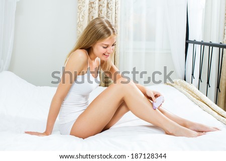 Blonde woman is  sitting on bed in her bedroom and waxing her legs,Waxing