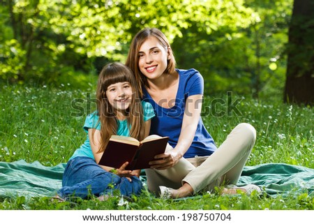 Little girl and her mother reading a book while they sitting and enjoy in beautiful nature,Mother and daughter reading a book