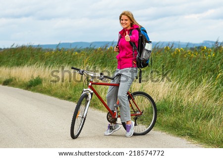Beautiful blonde woman standing on the country road with her bike and showing thumbs up,Thumbs up for cycling!