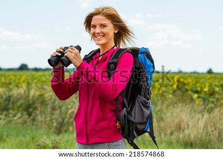 Cheerful blonde woman is standing in the nature and holding binoculars ,Enjoying nature with binoculars