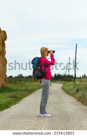 Woman is standing on the country road and  watching something through binoculars,Nature observation through binoculars