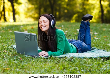 Beautiful young woman with headphones enjoys in music while lying down in nature,Enjoy music