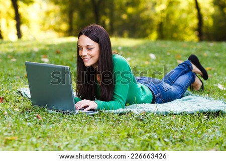 Young woman is using her laptop while lying down in the nature,Woman using laptop