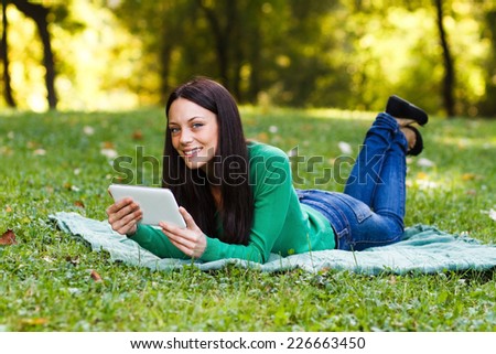 Young woman is using her digital tablet while lying down in the nature,Woman using digital tablet