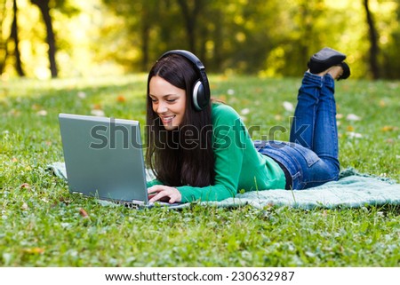 Young woman with headphones is using her laptop while lying down in the nature,Woman  with headphones using laptop
