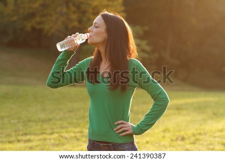 Beautiful woman is standing in the park and drinking water.Refreshment