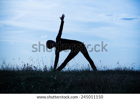 A silhouette of a woman practicing yoga,intentionally toned image.Yoga-Trikonasana right/Right triangle pose