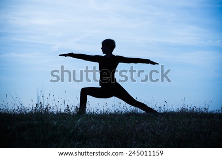 A silhouette of a woman practicing yoga,intentionally toned image.Yoga-Virabhadrasana /Warrior pose