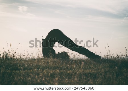 A silhouette of a woman practicing yoga,intentionally toned image.Yoga-Halasana/Plow pose