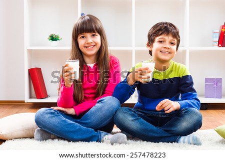 Cute little girl and little boy are holding glass of milk and looking at camera.We like to drink milk
