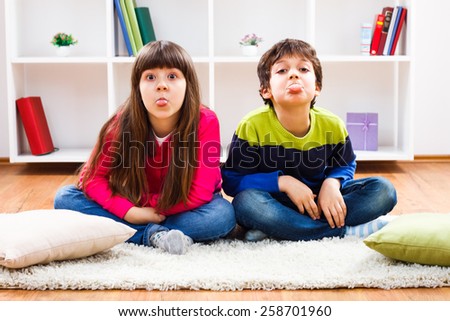 Little boy and little girl are sitting in living room and sticking out their tongue.Children sticking out tongue
