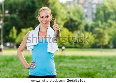 Beautiful blonde woman is standing in the park and giving thumbs up for exercise.Thumbs up for exercise