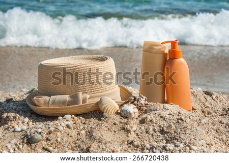 Photo of suntan lotion bottles and hat on the beach.Sun protection