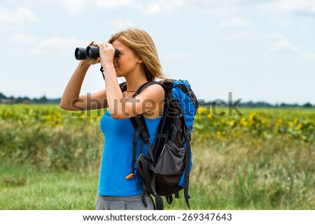 Woman is standing on the country road and watching something through binoculars .Enjoying in nature with binoculars