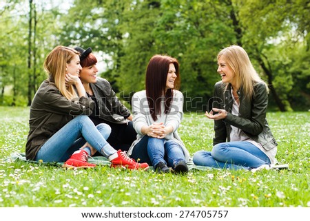 Four young girls sitting in the park and talking about something.Friends talking