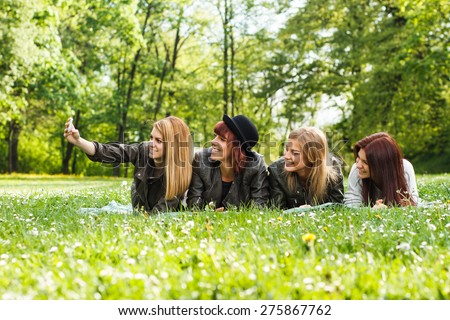 Four cheerful friends lying down in the park and taking photos of themselves with camera.\
Happy girls taking selfie
