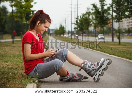 Portrait of cute young girl in roller skates resting and  using phone.Sporty girl using phone