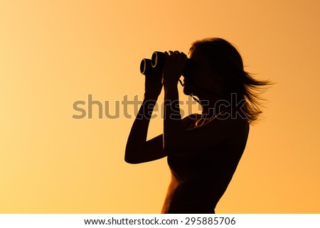 Silhouette of a woman standing and watching sunset with binoculars . Enjoying in sunset with binoculars