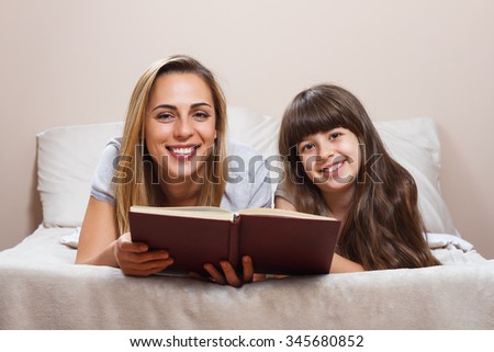 Mother and daughter reading together book in bed.Mother and daughter reading book