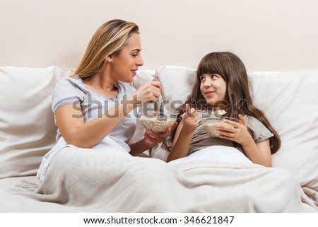 Mother and daughter are sitting on bed in pajamas,talking and having breakfast.Mother and daughter are talking and having breakfast
