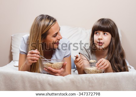Mother and daughter are lying on bed and talking about something while they having breakfast.Mother and daughter are talking and having breakfast
