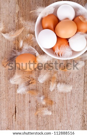 brown and white eggs in a bowl, feathers on rustic wooden table