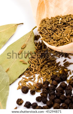 cumin on wooden spoon, black pepper, and bay leaves on white background