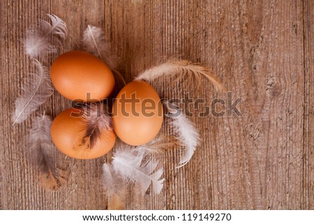 three eggs and feathers on rustic wooden table