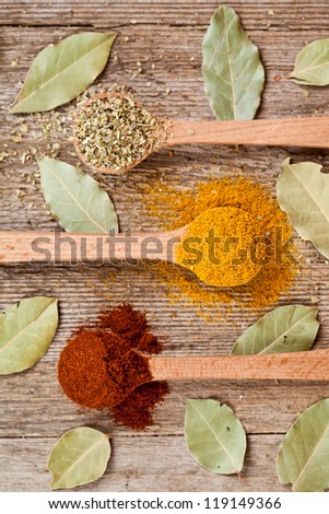 three spices in wooden spoons and bay leaves on rustic wooden background
