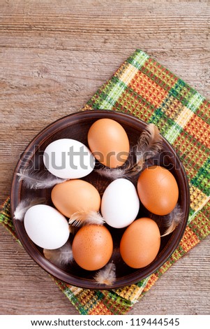 eggs in a plate, towel and feathers on rustic wooden table