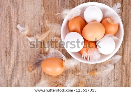 brown and white eggs in a bowl, feathers on rustic wooden table