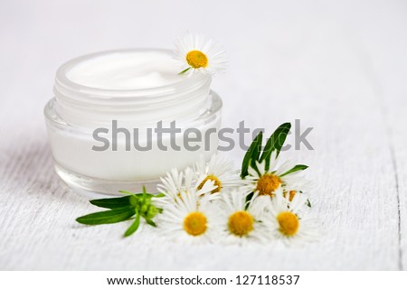 container with cream and chamomiles on white wooden  background