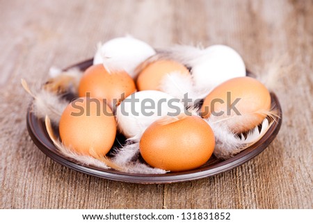 eggs and feathers in a plate on rustic wooden table