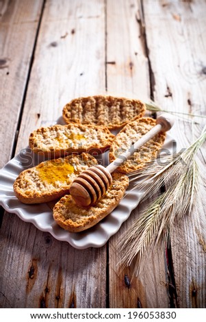 crackers with honey in plate and wheat ears on rustic wooden board