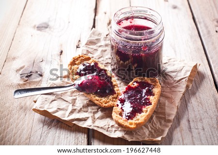 black currant jam in glass jar and crackers on rustic wooden board
