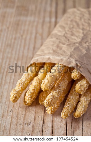 bread sticks grissini with sesame seeds in craft pack on rustic wooden background