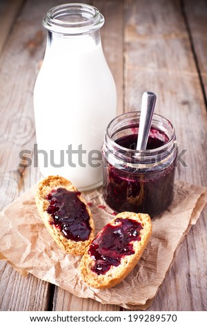 black currant jam in glass jar, milk and crackers on rustic wooden board