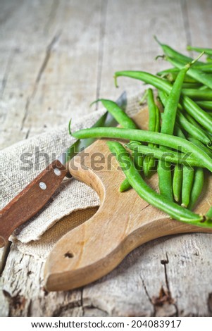 green string beans and knife closeup on wooden board